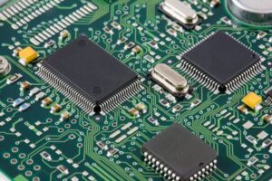 Close-up view of a green printed circuit board with multiple microchips, electronic components, and connecting tracks.