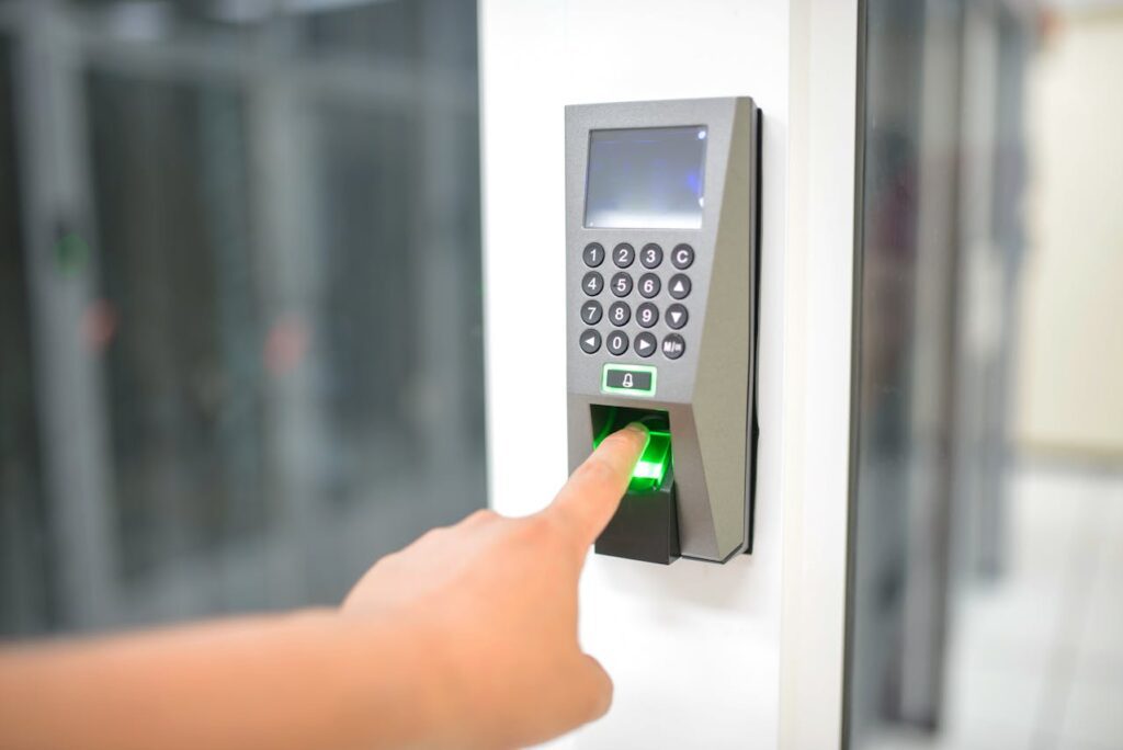 A person is pressing their finger on a biometric fingerprint scanner attached to a wall—a cutting-edge access authentication system used in defence electronics manufacturing.