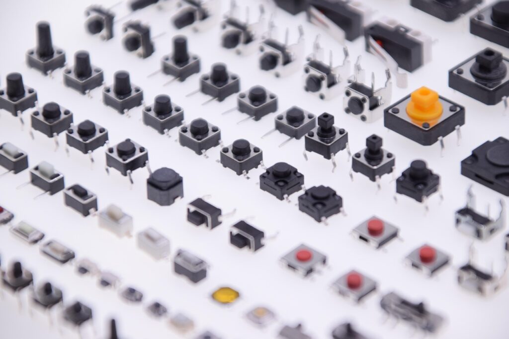 Assorted tactile switches and push buttons—ideal for defence electronics manufacturing—arranged in rows on a white surface, showcasing various shapes, sizes, and colours.