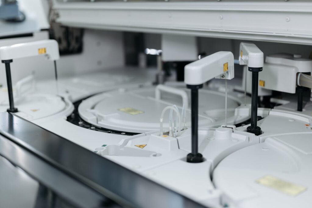 Close-up view of an automated laboratory analyser used for measuring and testing, featuring multiple sample compartments and robotic arms—essential in modern electronics manufacturing and scientific analysis.